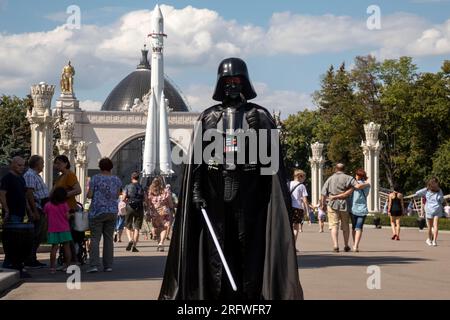 Moscow, Russia. 5th of August, 2023. A man dressed as the character of the Star Wars saga Darth Vader walks along a alley of the VDNKh exhibition center against a background of a Vostok carrier rocket on a hot summer day in the city of Moscow, Russia Stock Photo