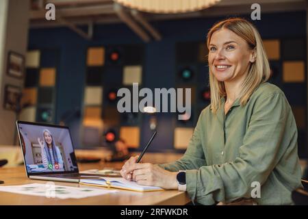 Smiling business woman is making notes during video conference in coworking. Distance work concept Stock Photo