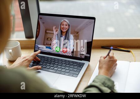 Close up of woman freelancer have video conference with client and making notes sitting near window Stock Photo