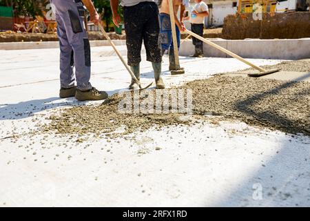 Construction workers, riggers are using rake and wooden handmade handcraft tool to spreading, leveling concrete covering white isolation, fabric, pour Stock Photo