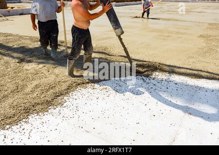 Construction worker is directing the pump tube on right direction, pouring layer of concrete in building foundation covering white isolation, fabric, Stock Photo