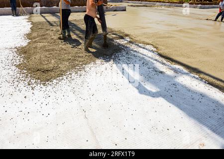 Construction worker is directing the pump tube on right direction, pouring layer of concrete in building foundation covering white isolation, fabric, Stock Photo