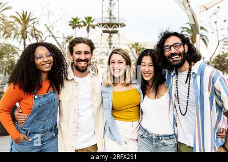 Group of cheerful millennial friends together hugging each other in street. Happy multiracial young hipster friends laughing and having fun outside Stock Photo