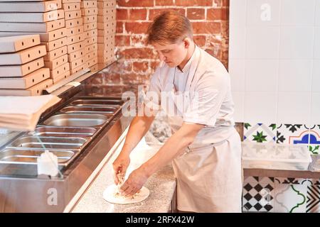 Raw pizza ready to bake. The chef prepares pizza. boxes for food delivery on background. Neapolitan pizza from a wood-fired oven.  Stock Photo