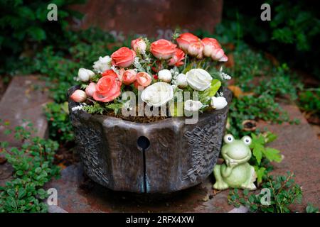 a brown pot with white and red artificial roses as grave decoration on a cemetery Stock Photo