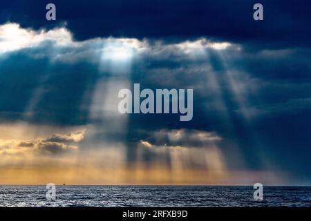The sun breaks through the clouds illuminating the sea with its rays Stock Photo