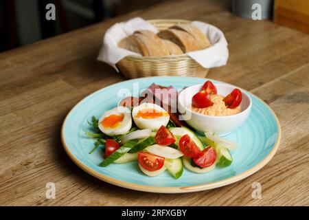 Soft Boiled eggs with vegetables, ham and sausage on a plate with bread on the side Stock Photo