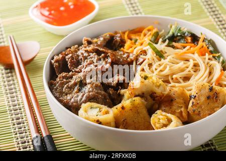Vietnamese Beef Noodle Salad Bun Bo with crispy nem spring rolls and vegetables closeup on the table. Horizontal Stock Photo