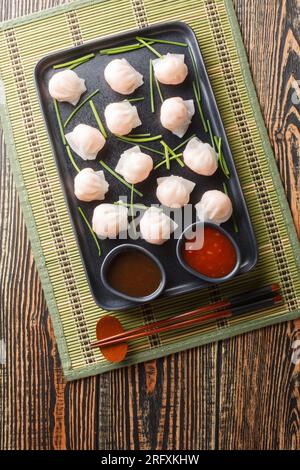 Chinese Har Gow Dim Sum dumplings in the shape of a bonnet served with sauce on the table. Vertical top view from above Stock Photo