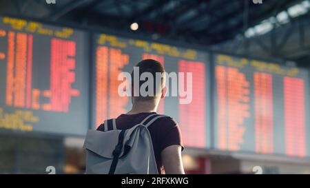 Traveling by airplane. Rear view of man walking through airport terminal against flight information board. Stock Photo