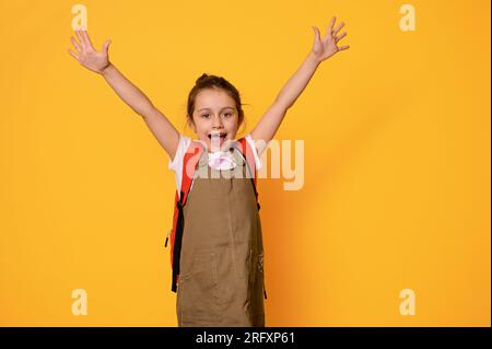 Authentic portrait of Caucasian elementary age girl, school child dressed in casual wear, expressing positive emotions, isolated on orange studio back Stock Photo