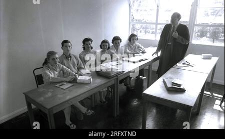 1950s, historical picture, young students sitting in a line at desks in a classroom, with an elderly male Professor, wearing a formal gown, standin by them, Witney, Oxon, England, UK. Stock Photo