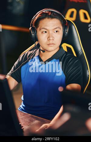 Professional cybersport gamer. Portrait of a young asian guy wearing headphones looking aside while participating in eSport tournament Stock Photo
