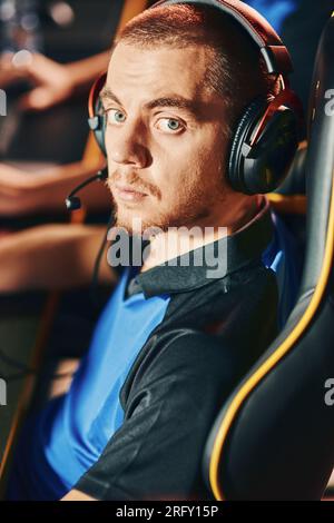 Portrait of a young caucasian guy wearing headphones looking at camera while participating in eSport tournament, sitting in gaming club or internet Stock Photo