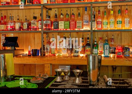 A well stocked bar indoors with a variety of liquors to choose from displayed on shelving on the back wall with lighting behind the bottles and other Stock Photo