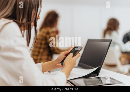 The woman is using her mobile phone for business purposes, such as making calls, sending emails, and checking her calendar Stock Photo