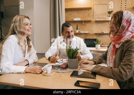 Inter-generational businesspeople having fun conversation while working together at the cafe. Muslim female employee telling a fun story Stock Photo