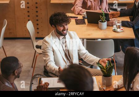 Disabled male business person in wheelchair discussing with his coworkers during meeting at the office. Disability concept Stock Photo