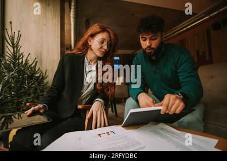 Two businesspeople, gorgeous ginger woman and handsome bearded man, working remotely on a new project at the coffee bar. Working in good atmosphere Stock Photo