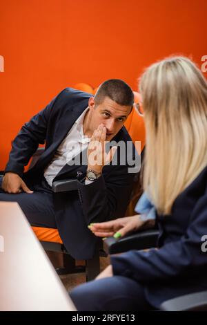 Two young and well-dressed students talking and smiling while attending a lecture Stock Photo