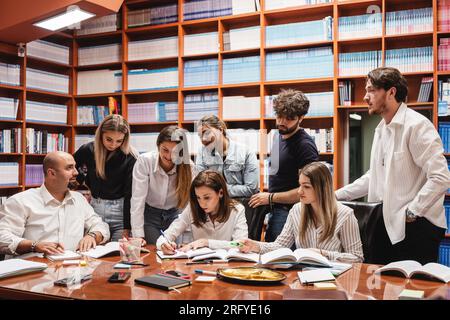 Two professors explaining and talking to a young group of students in the library Stock Photo