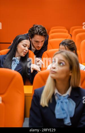 Three students looking at a phone, talking and not paying attention in class Stock Photo