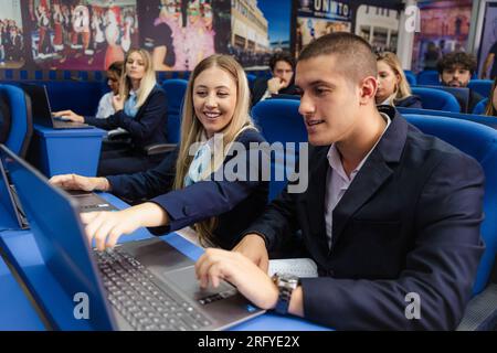 Young and well-dressed students smiling and working together on their laptops in class Stock Photo