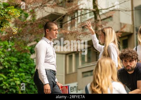 Two young and well-dressed students standing outside, talking and discussing Stock Photo