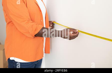 Black Man Taking Measurements With Tape Ruler On White Wall Indoors Stock Photo