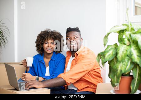 Black Couple Using Laptop And Planning Design In New Flat After Moving Stock Photo