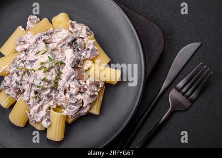 Delicious fresh pasta with champignon mushrooms in a creamy sauce with salt, spices and herbs on a dark concrete background Stock Photo