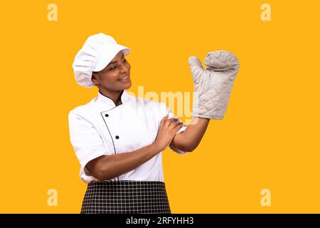 Happy Black Chef Woman Looking At Oven Mitt On Her Hand Stock Photo
