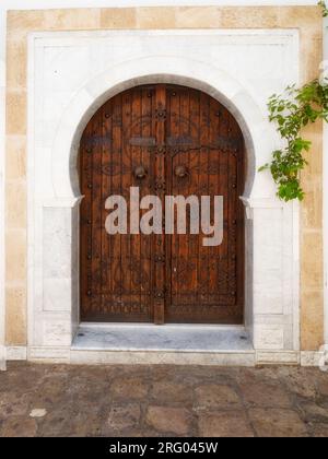 Traditional arched wooden door with decorative knockers on a white facade in Sidi Bou Said, Tunisia. Stock Photo