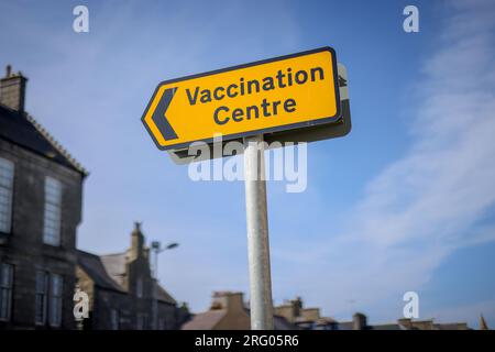 Yellow COVID-19 'Vaccination centre' sign against blue sky. Taken in Fraserburgh, North East Scotland. Stock Photo