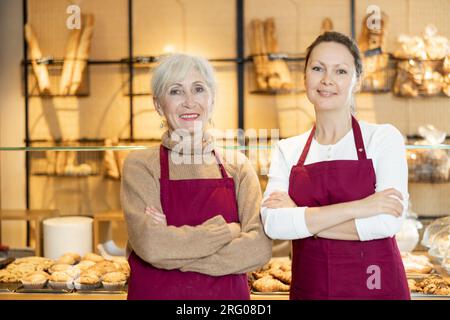 Smiling female bakers in maroon aprons standing with crossed arms Stock Photo