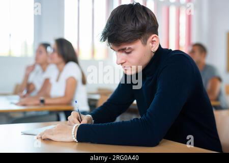 Focused guy listening and taking notes of lecture in university classroom Stock Photo