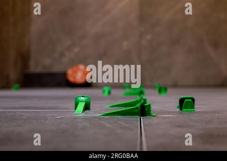 Tile levelling system, four plastic green clips with wedges. Close-up view, selective focus, blurred background. Stock Photo