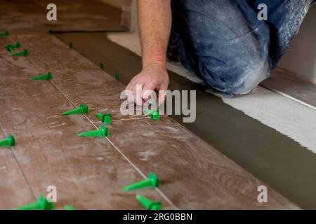 Close up hands of repairman laying tiles with tile leveling system on the floor in a new house. Stock Photo