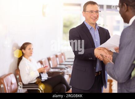 Middle-aged man handshaking with other person in waiting room Stock Photo