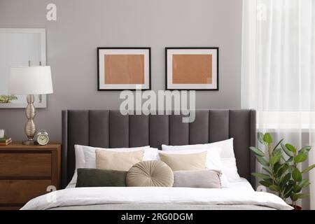 Comfortable bed with cushions, lamp and different decor on wooden chest of drawers in room. Stylish interior Stock Photo