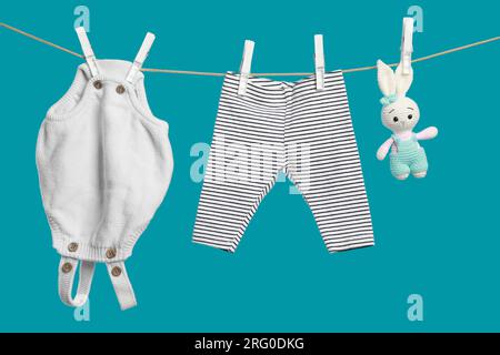 Baby clothes and crochet toy drying on washing line against turquoise background Stock Photo