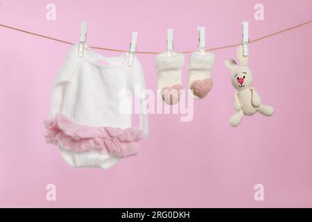 Baby clothes and handmade toy drying on washing line against pink background Stock Photo