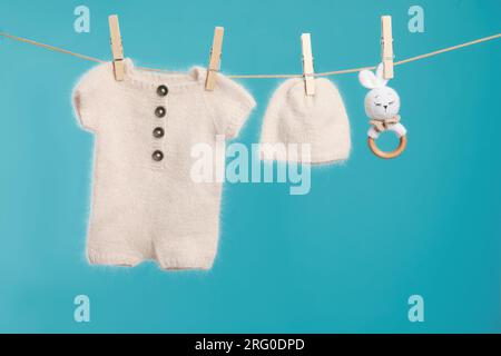 Knitted baby clothes and handmade toy drying on washing line against turquoise background Stock Photo