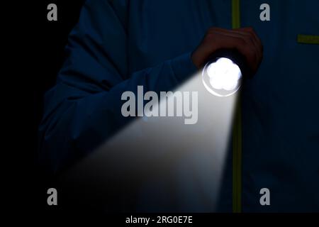 Man with bright flashlight in darkness, closeup Stock Photo