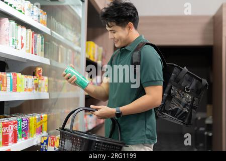 Grocery delivery service shopper with insulated delivery bag buying items for customers at supermarket. Asian man rider selecting food supply for client order Stock Photo