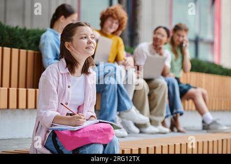 back to school, happy girl taking notes near teen classmates and teacher, blur, diversity, study Stock Photo