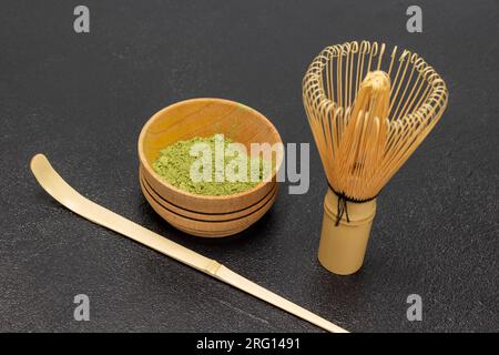 Green Matcha tea powder in a wooden bowl. Bamboo whisk and spoon on the table. Top view. Black background Stock Photo