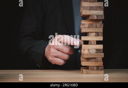 Businessman hand of businessman pulling out or placing wood block on the tower with copyspace. Business risk, strategy and planing concept idea. Stock Photo