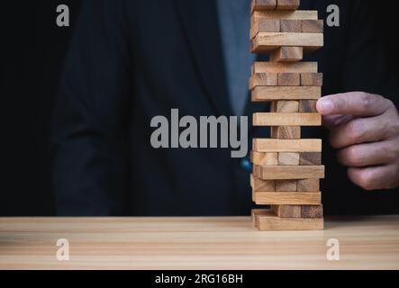 Businessman hand of businessman pulling out or placing wood block on the tower with copyspace. Business risk, strategy and planing concept idea. Stock Photo