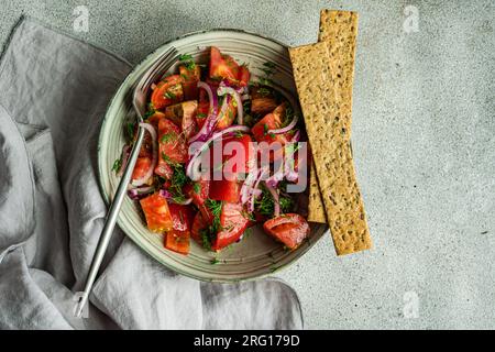 From above of bowl with salad made of tomatoes red onion and dill herb placed near on marble table Stock Photo